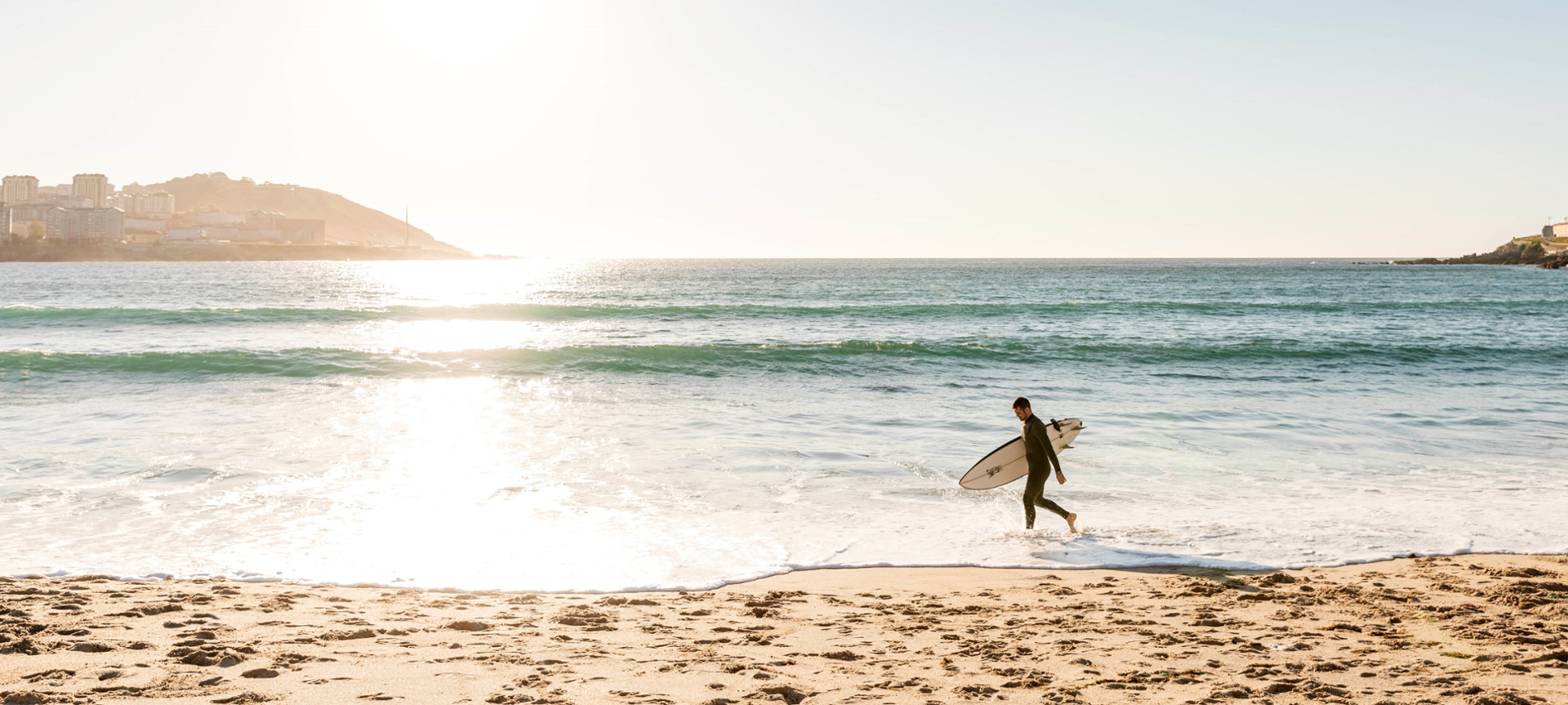 Surfeiro paseando pola praia cunha táboa de surf debaixo do brazo