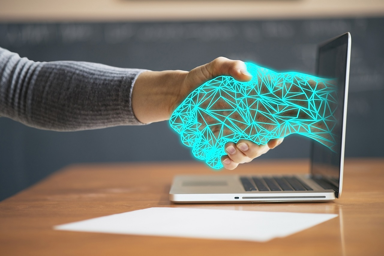 Grafismo de una mano humana saludando a una mano virtual que sale de un ordenador