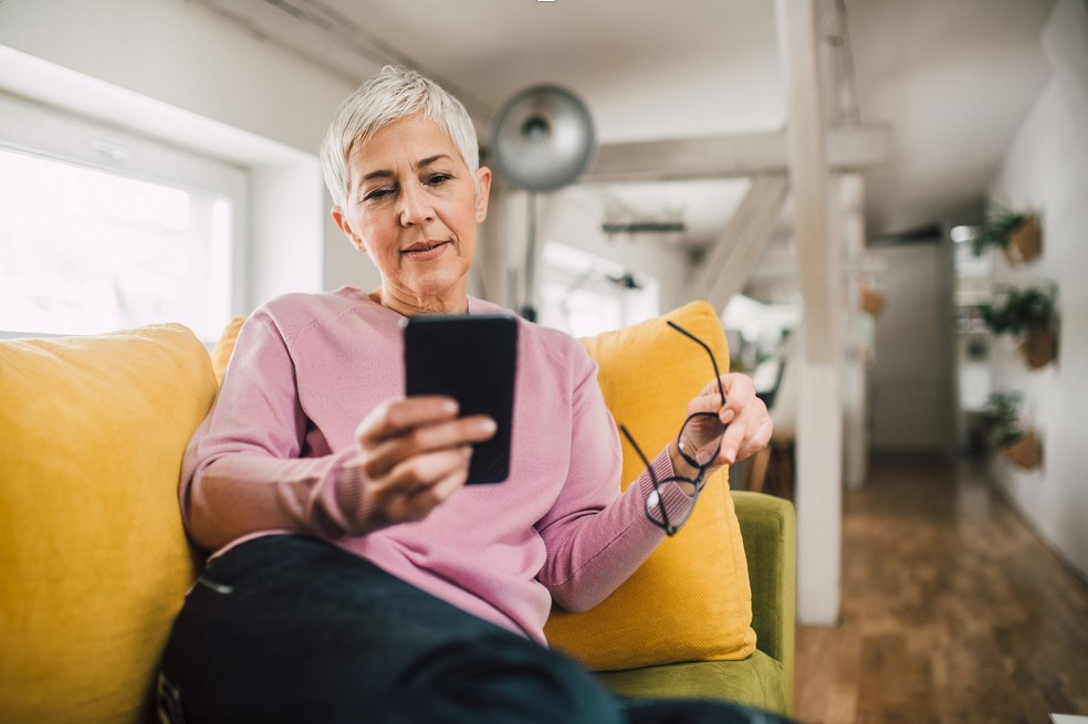 Una mujer madura mira un móvil en un sofá de una casa